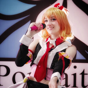Ghosty cosplaying as Freyja from Macross Delta, wearing an orange and yellow wig and a colorful cosplay.